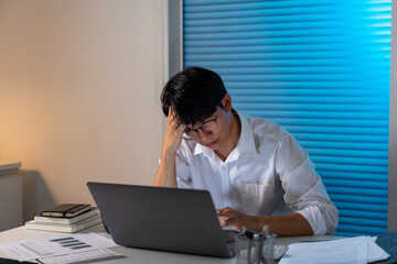 Overwork Concept The male officer resting his forehead on his right hand while working late at his...