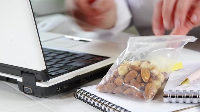 Healthy snack video. Diet and healthy lifestyle. A girl or a woman, a close-up angle in the frame works with a laptop, takes a snack of nuts from the table.