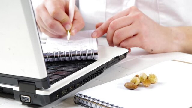 Healthy snack video. Diet and healthy lifestyle. A girl or a woman, a close-up angle in the frame works with a laptop, takes a snack of nuts from the table.