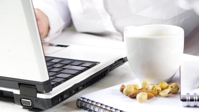Healthy snack video. Diet and healthy lifestyle. A girl or a woman, a close-up angle in the frame works with a laptop, takes a snack of nuts from the table.