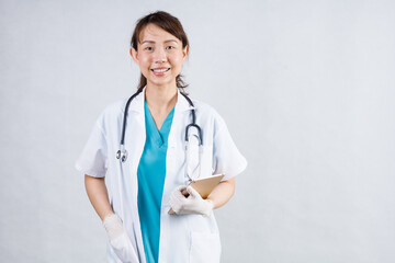 Smiling asian woman physician in a white coat over gray background