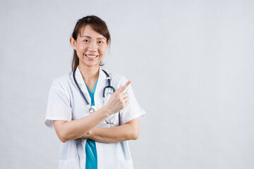 Smiling asian woman physician in a white coat over gray background