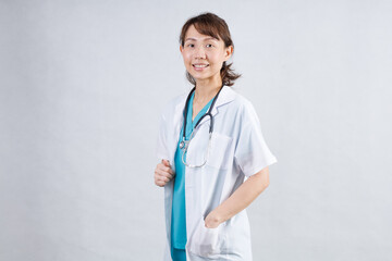 Smiling asian woman physician in a white coat over gray background