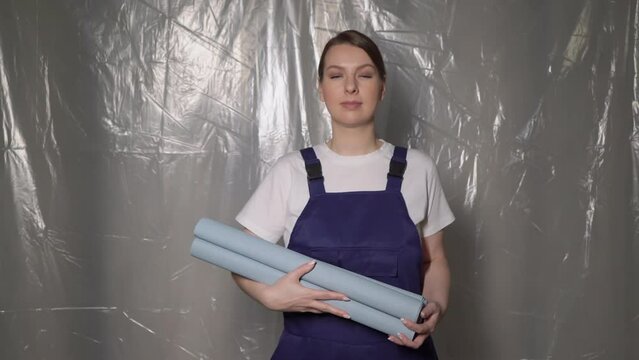 Woman builder in blue overalls with roll of blue wallpaper.