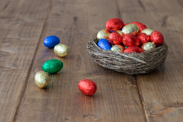 colorful wrapped chocolate easter eggs in a brown nest on a wooden rustic table