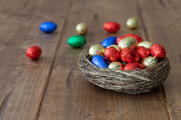 colorful wrapped chocolate easter eggs in a brown nest on a wooden rustic table
