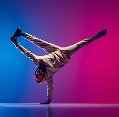 Studio shot of young flexible sportive man dancing breakdance in white outfit on gradient pink blue...