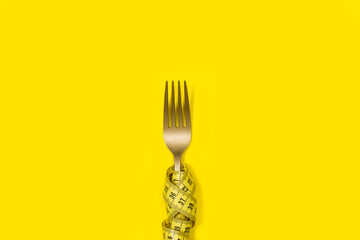 Tenedor dorado con cinta métrica amarilla sobre un fondo amarillo liso y aislado. Vista superior y...