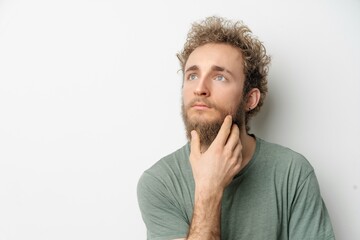 Thoughtful or pensive young handsome bearded wild curly hair man with bright blue eyes isolated on...