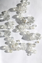 Various transparent beads on white background, illuminated by sunlight and reflectiing light. Flat lay.