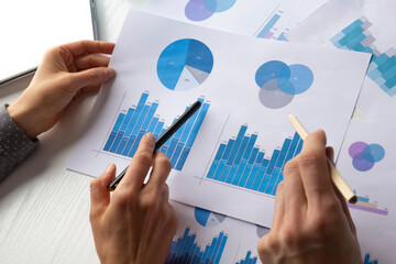 The hands of a financial analyst hold sheets with graphs, statistical reports.