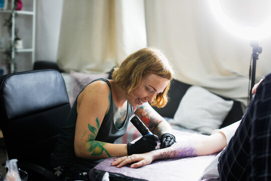 Tattoo parlor, pretty European red-haired girl makes a tattoo on arm. Woman creates a tattoo on a female hand by a professional tattoo artist