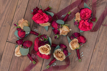 Wedding butonnieres on wood table. Red and blush weding corsages.
