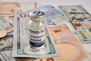 Covid vaccine vial - photo on cash bills. Coronavirus vaccine glass bottle is placed on cash bills. Euro and dollar banknotes as background under coronovirus inoculation remedy. Antivirus cure cost.