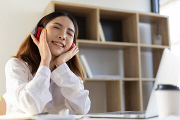 Girl at home using laptop and wearing headphones listening to music. © Wasan