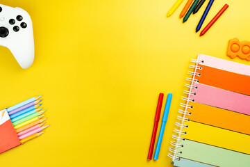 Fototapeta premium Back to school. School supplies on a yellow background. Children's multi-colored accessories like crayons, notebook, scissors, video game controller. Space for text. Top view