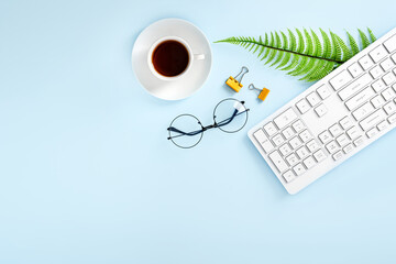 Obraz na płótnie Canvas Stylish office desktop with keyboard, cup of tea, glasses and a plant on a blue background, top view, copy space