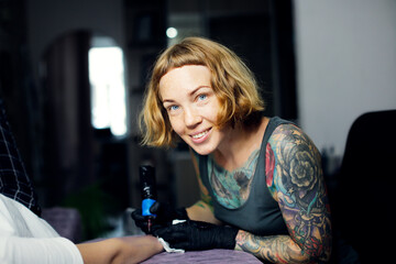 Tattoo parlor, pretty European red-haired girl makes a tattoo on arm. Woman creates a tattoo on a...