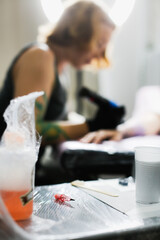 Tattoo parlor, pretty European red-haired girl makes a tattoo on arm. Woman creates a tattoo on a female hand by a professional tattoo artist