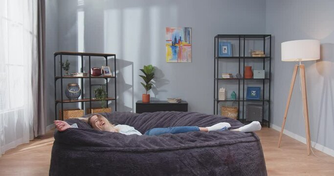 Full size shot on young active caucasian woman jumping on her side on soft sofa and lyong smiling. Happy, carefree people concept. Slowmotion video.