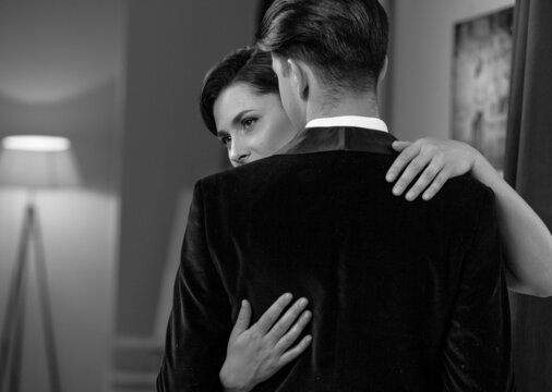 Dancing passion woman hugs man standing back to camera. Husband and wife after a romantic dinner. Romance in relationships. Beautiful young couple in home interior. Black and white photo