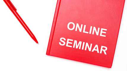 The text ONLINE SEMINAR is written on a red notepad near a red pen on a white table in the office. Business concept