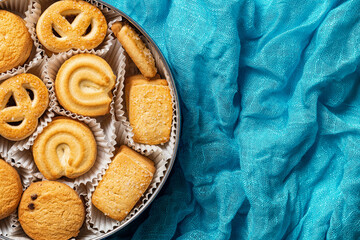 Tasty danish butter cookies in a tin over crumpled turquoise cloth. Open container with assorted shortbread biscuits. Baked pastry, breakfast concepts. Sweet food and calories. Copy space.