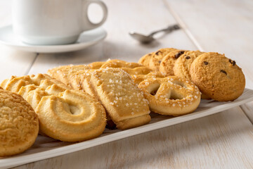 Set of danish butter cookies on a white rectangular plate and coffee cup. Assorted crispy shortbread biscuits and teacup close-up. Baked pastry for breakfast, sweet food concepts.