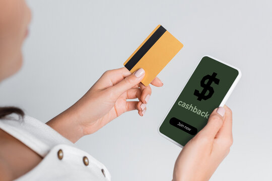 partial view of woman using mobile phone with cashback on screen and holding credit card isolated on grey.