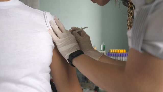 Nurse in gloves making a vaccine injection to hand of male patient in health clinic. Medic giving Covid-19 or flu antivirus vaccine shot to patient from virus disease at hospital. Vaccination concept