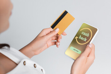 partial view of woman holding mobile phone with cashback on screen and credit card isolated on grey.