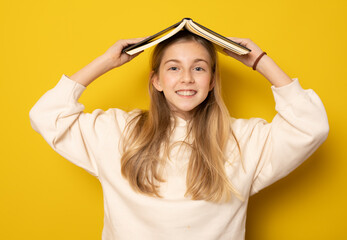 Fototapeta na wymiar Beautiful girl with a book on her head isolated over yellow background. Education concept.