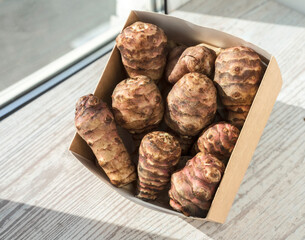 Jerusalem artichoke tubers in a cardboard box on a wooden windowsill