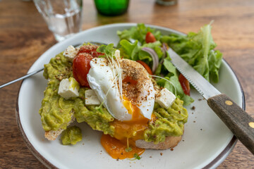 Sourdough toast, poached eggs, avocado pulp and fresh vegetables on plate in cafe, close up