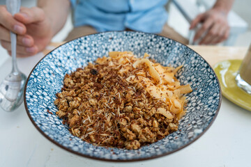 Bowl with granules and coconut and chocolate chips for a healthy breakfast. Male hand with a spoon and a plate with muesli