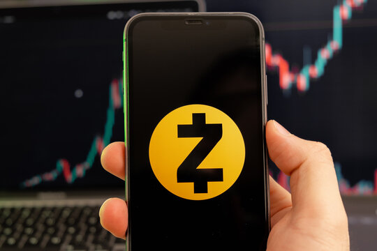 Zcash ZEC cryptocurrency logo on the screen of a smartphone in mans hand with a growing trend on the chart on a green background.