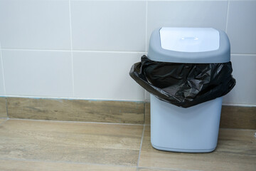 a blue trash can with a black bag stands in the interior