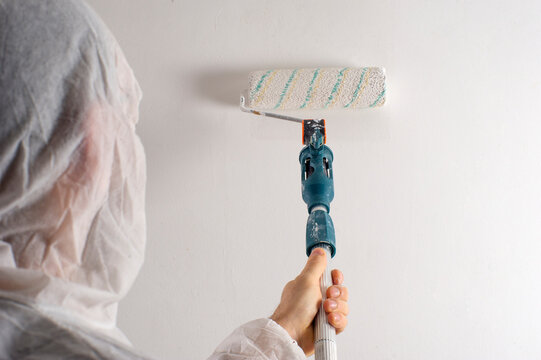 Hompre pintando habitaci&oacute;n blanca, pintar pared con rodillo y mono protector un solo uso