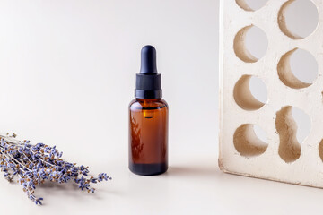 bottle with a pipette, lavender branches and a brick on a beige background
