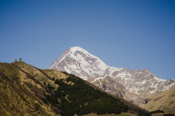A beautiful mountain landscape with a blue sky and a church. Snow-capped peak of Mount Kazbek in Stepantsminda Georgia