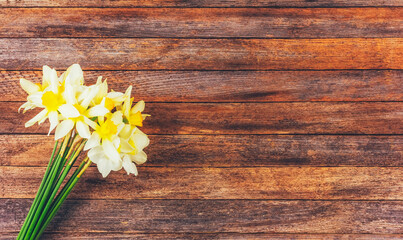 a bouquet of narcissus flowers on a brown wooden background with a copy space