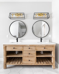 A modern farmhouse bathroom with a natural wood vanity cabinet, black and gold light fixtures above...