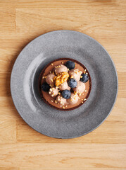 Round chocolate tart with chocolate cream. creme brulee, blueberry and nuts on a plate on a wooden background. Pie with milk chocolate and roasted walnuts. Top view. Copy space. Creme brulee ice cream