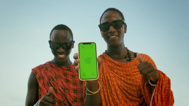 Extremely Happy, Satisfied Masai Tribe Men Showing Green Screen on Smartphone to the Camera and Making Thumb Up Sign. Masai Mara Likes New Mobile Phone App. Commercial Ad Concept. Slowed Down x2