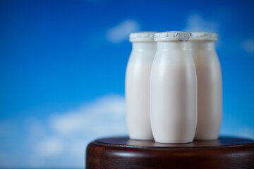 Natural liquid yogurt with probiotics in small plastic bottles on wooden table on background of blue sky with clouds. Healthy, balanced diet food, healthy breakfast, dairy products.