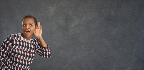 Young funny and inquisitive dark-skinned woman on a gray background overhears a conversation. Woman...