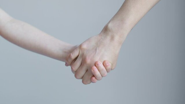 Woman and child join hands and hold in front of the background of a white wall