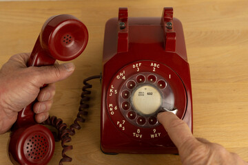 A man using a vintage red rotary telephone - obrazy, fototapety, plakaty