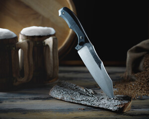 large tactical knife with a wide blade and a handle made of testolite is stuck into a piece of wood...