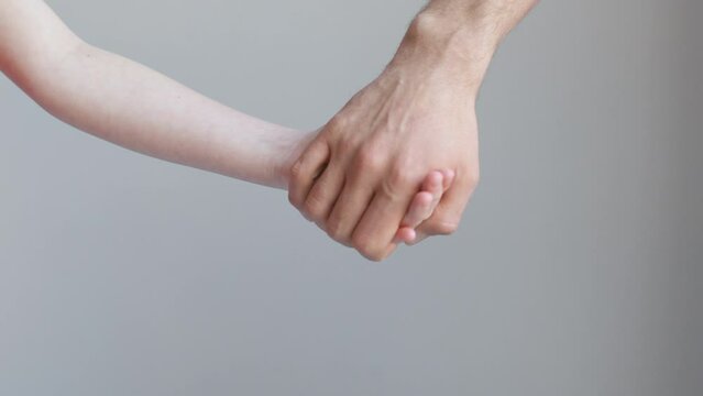 Man and child join hands and hold against the background of a white wall